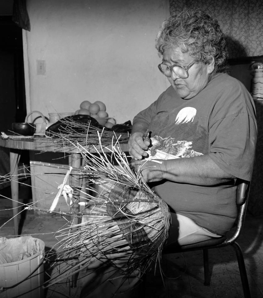 Evelyn Seletstewa pushing down on the wefts of a wicker fruit basket