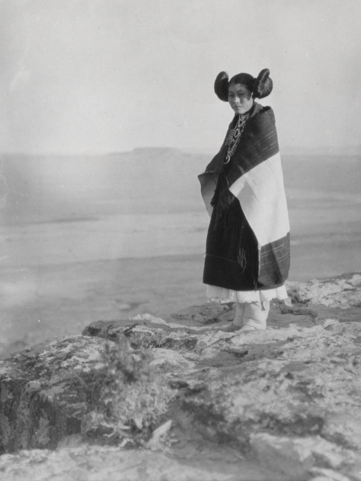 Girl dressed in traditional manta etc., standing near edge of cliff